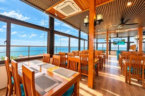 Ein Restaurant mit Holztischen und großen Fenstern mit Blick auf das Meer.