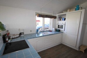 A kitchen with a black stovetop, white cabinets, a sink, and a window. - Top Wadden Sea holiday home (Esbjerg)