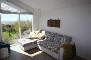 A room with a large window, a sofa, a small table, and a wall-mounted shelf. - Top Wadden Sea holiday home (Esbjerg)
