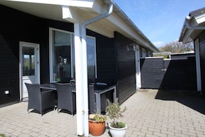 An outdoor patio area with a table and chairs, a potted plant, and a building with a dark exterior. - Top Wadden Sea holiday home (Esbjerg)