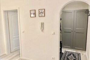 Un couloir avec une porte blanche, un porte-manteau et une armoire grise.
