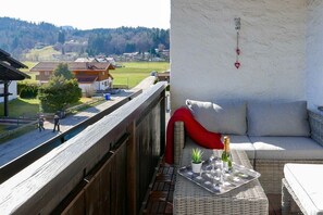 Ein Balkon mit einer Rattan-Couch, einem kleinen Tisch mit Flasche und Gläsern sowie Blick auf ein Dorf.