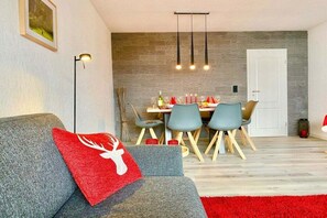 Ein modernes Wohnzimmer mit einem grauen Sofa, einem roten Kissen und einem Essbereich mit Tisch für vier Personen.