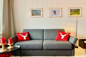 Ein graues Sofa mit zwei roten Kissen, ein kleiner Tisch mit Kerzen und drei gerahmte Bilder an der Wand.