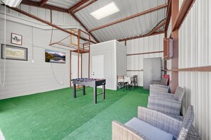 Une pièce avec une table de baby-foot, des meubles en osier et une moquette verte.