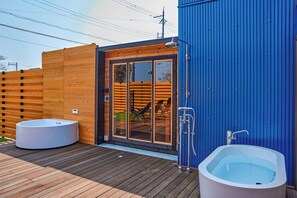 Casa de banho exterior moderna com deck de madeira, entrada por porta de vidro e parede azul.