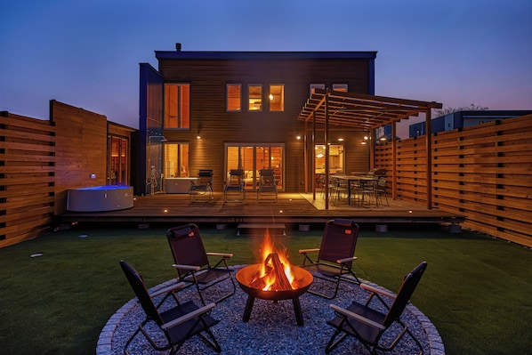 Una casa moderna con un patio que cuenta con una fogata y mobiliario exterior.