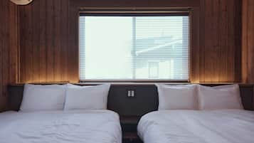 A room with two beds, wooden walls, a window with blinds, and a thermostat on the wall.