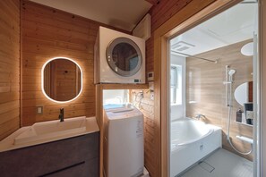 A modern bathroom with a wooden interior, a round mirror, a built-in washing machine, a bathtub, and a shower area. - IZA moriyama (Moriyama-shi)