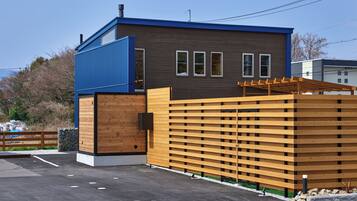 A modern building with a blue and brown exterior, a wooden fence, and a paved parking area.