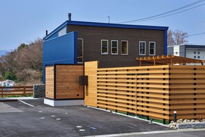 Um edifício moderno com fachada azul e marrom, cerca de madeira e estacionamento pavimentado.