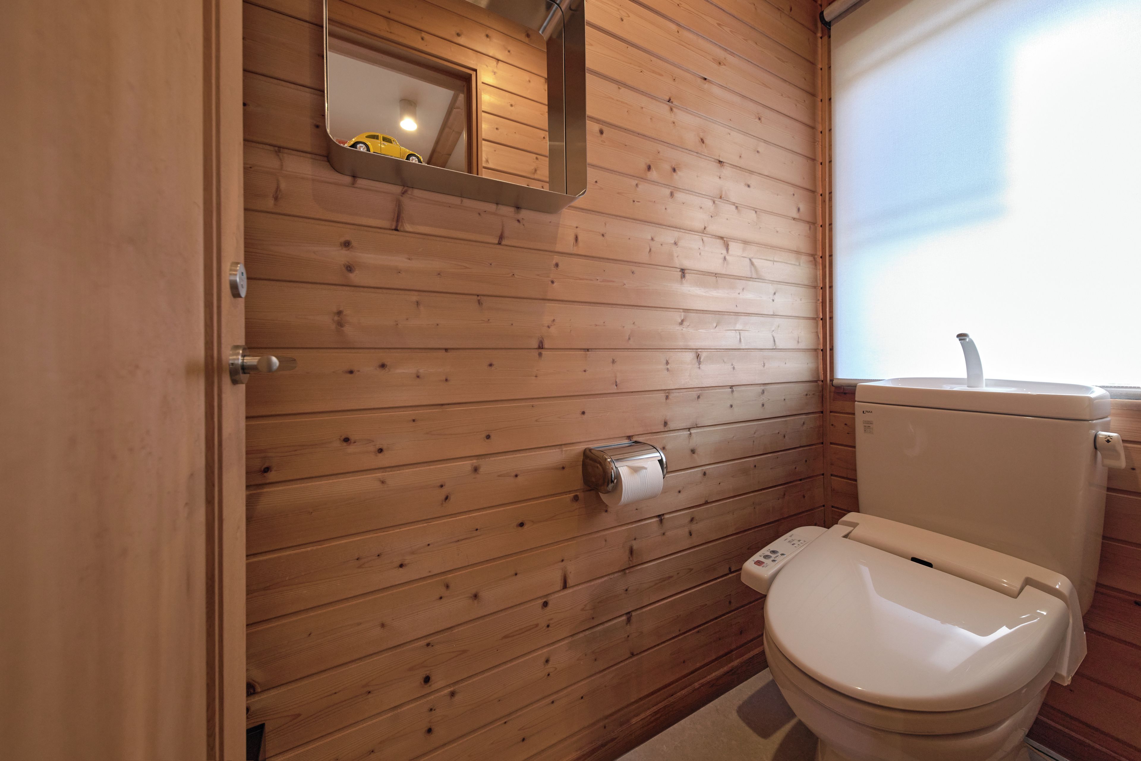 A wooden-paneled bathroom with a toilet, a paper towel dispenser, and a mirror.