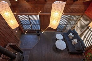 A modern interior with a wooden ceiling, a sofa with cushions, two round tables, and a large window with a view.