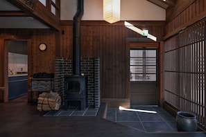 A room with a wood-burning stove, a kitchen area with a sink and shelves, and a sliding door leading to another space.