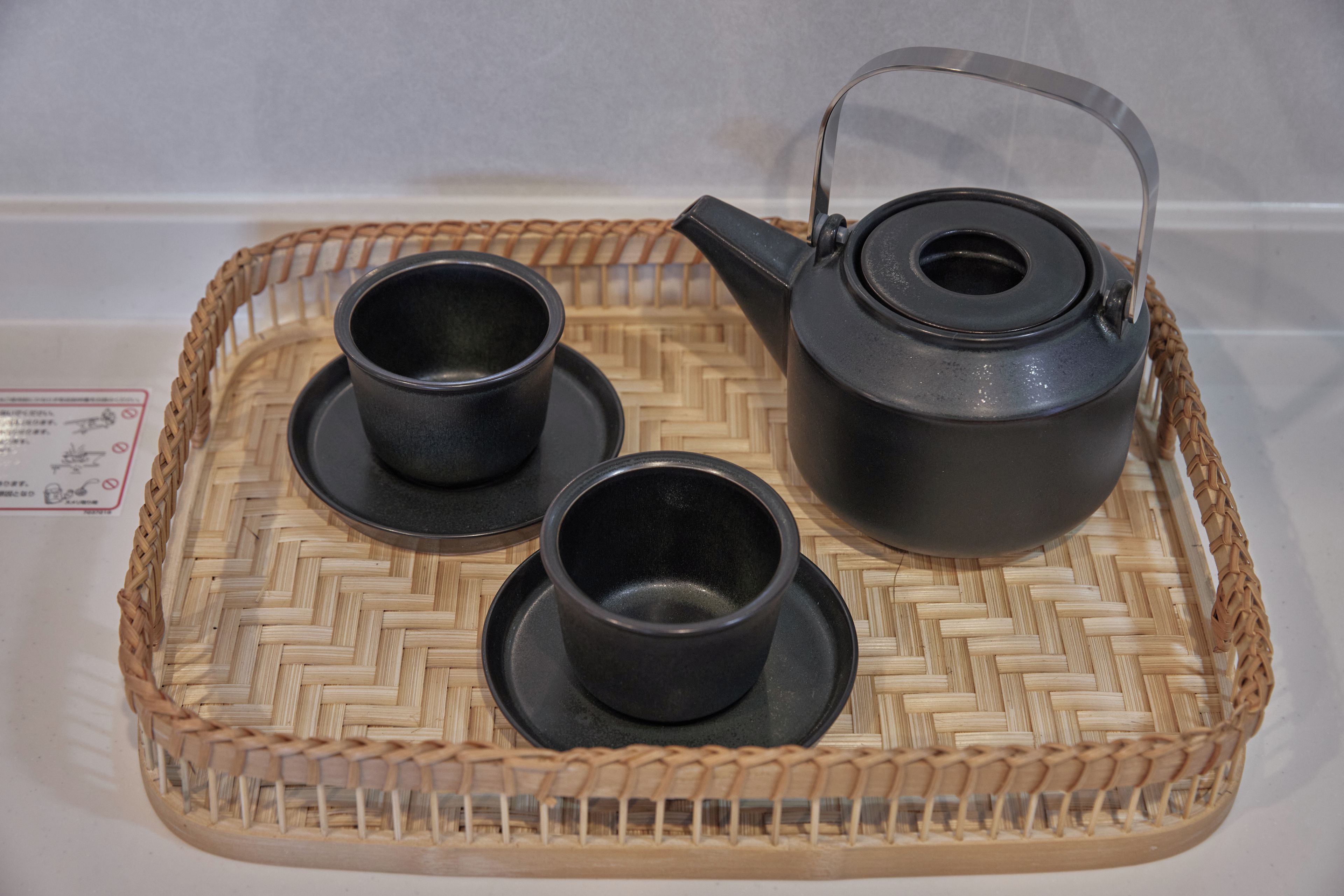 Una bandeja con un hervidor negro y dos tazas negras sobre un tapete tejido.