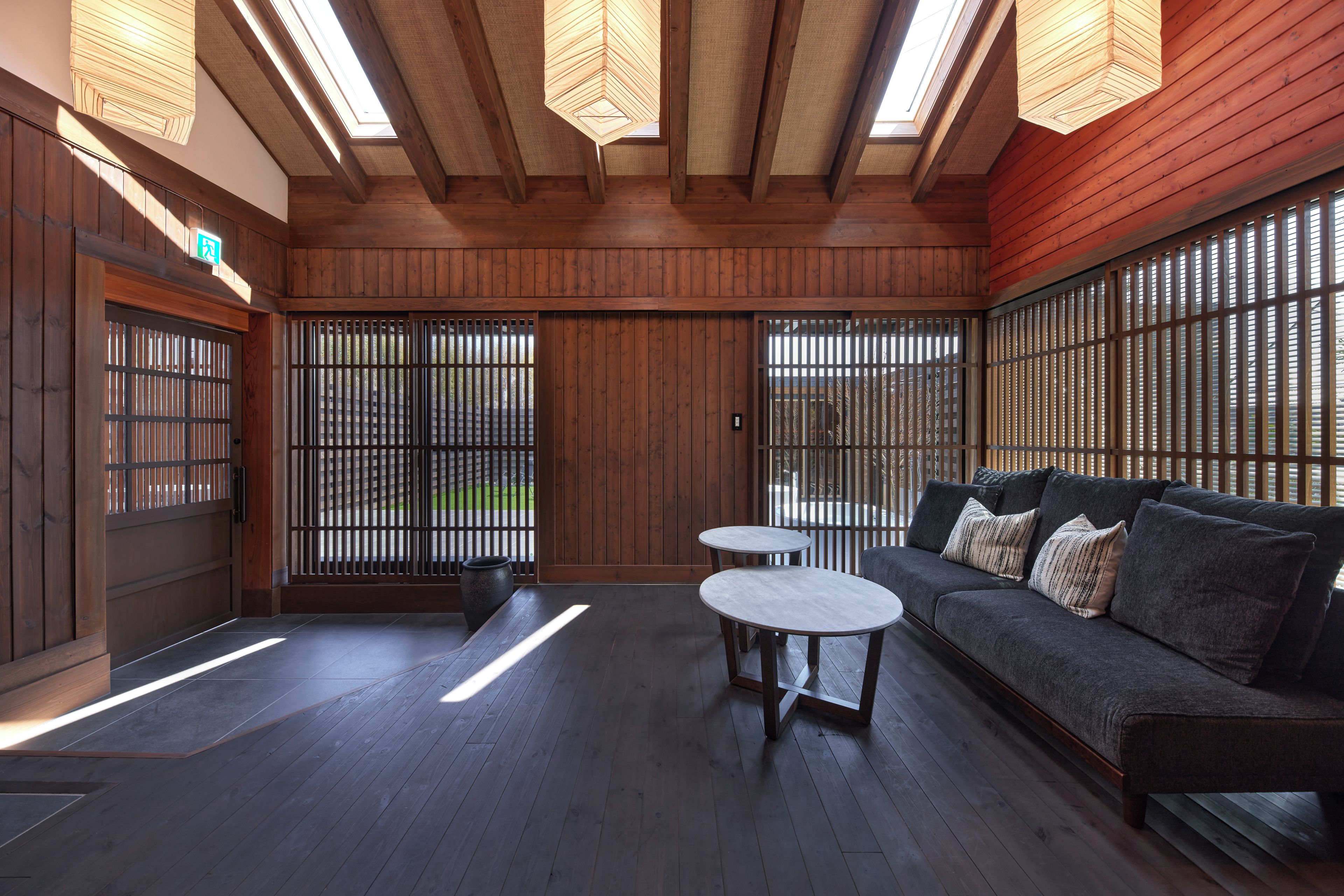 A room with a wooden ceiling, a sofa, two round tables, and a view through a shoji screen.