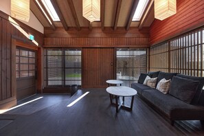 Quarto com teto de madeira, um sofá, duas mesas redondas e vista através de um painel shoji.