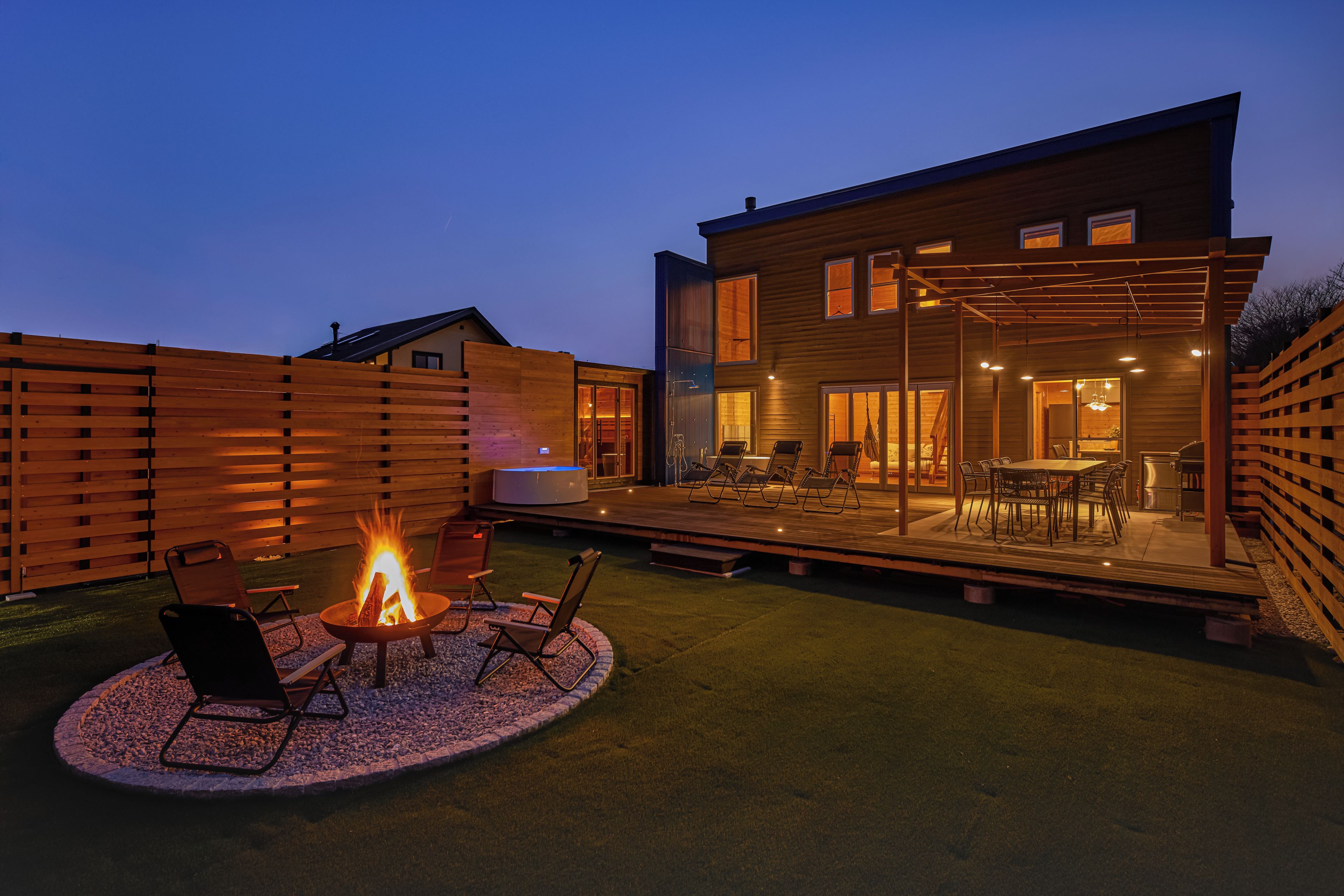 A modern outdoor patio with a fire pit, seating, and a dining area.