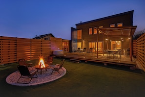 Un patio moderno al aire libre con un pozo de fuego, asientos y una zona de comedor.