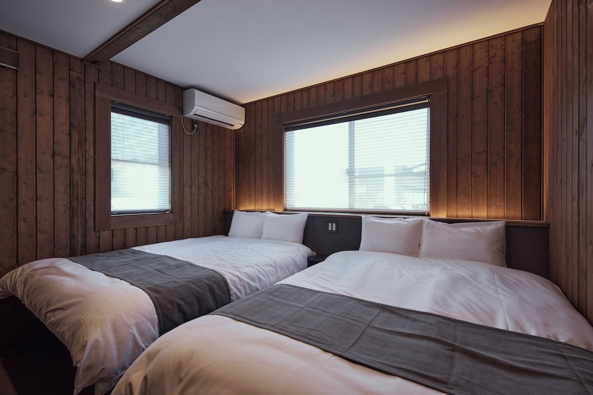 Una habitación con dos camas, paneles de madera y ventanas amplias.