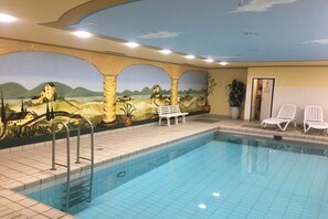 Ein Swimmingpool mit Wandgemälde, Liegestühlen und einer Bank.