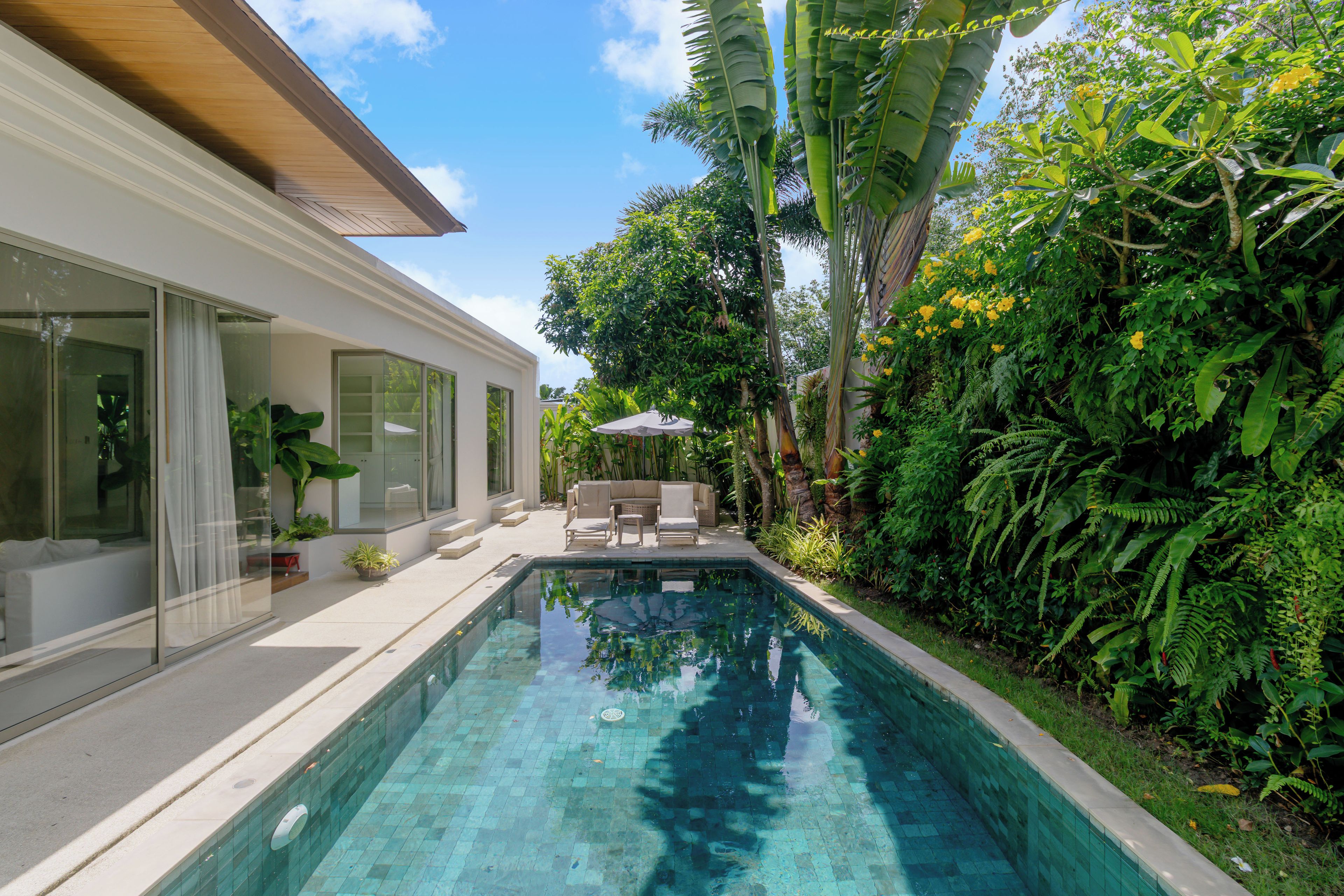 Una casa moderna con piscina, puertas de cristal y un patio con mobiliario exterior.