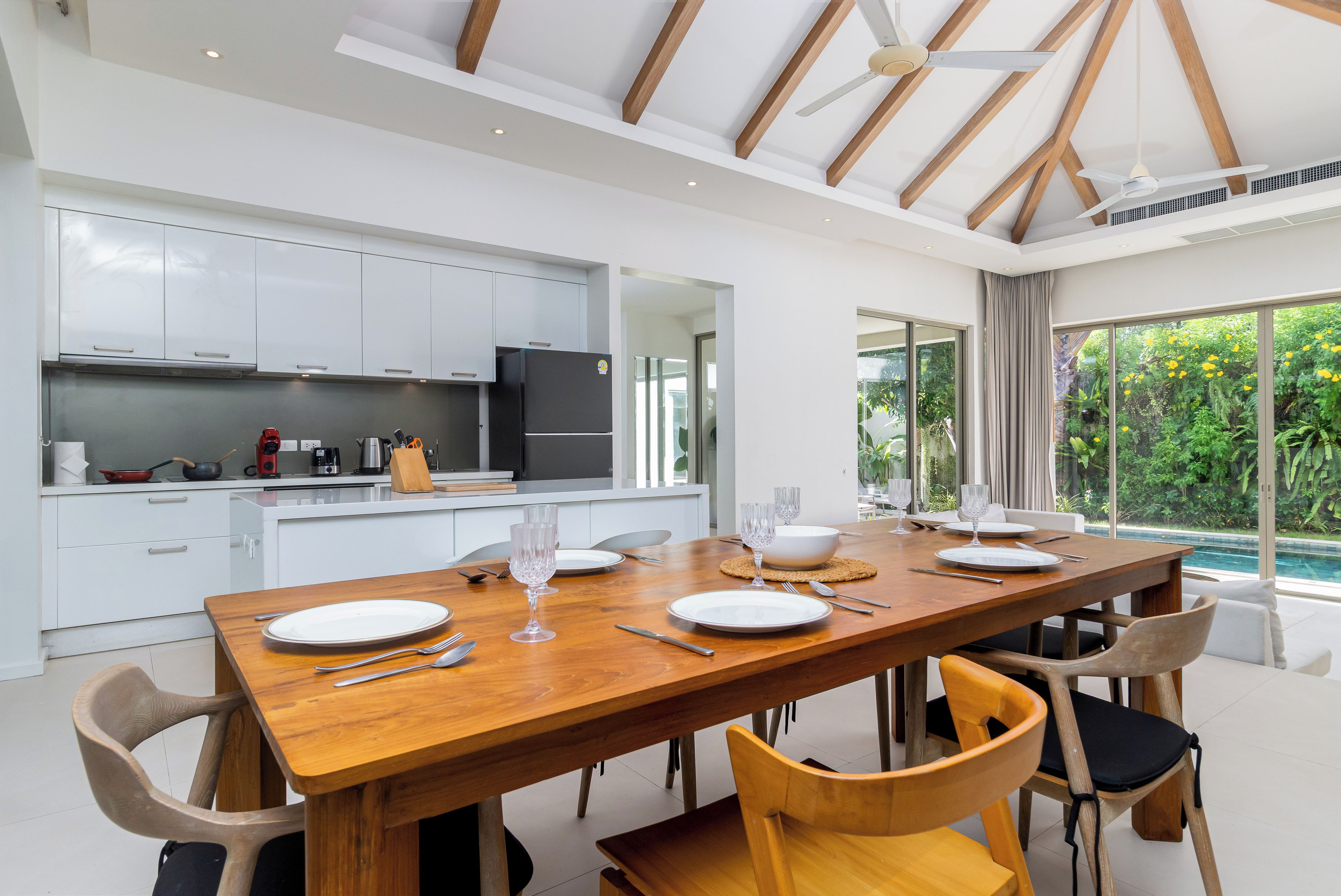 Una cocina moderna con armarios blancos y un comedor con una mesa de madera para cuatro comensales.