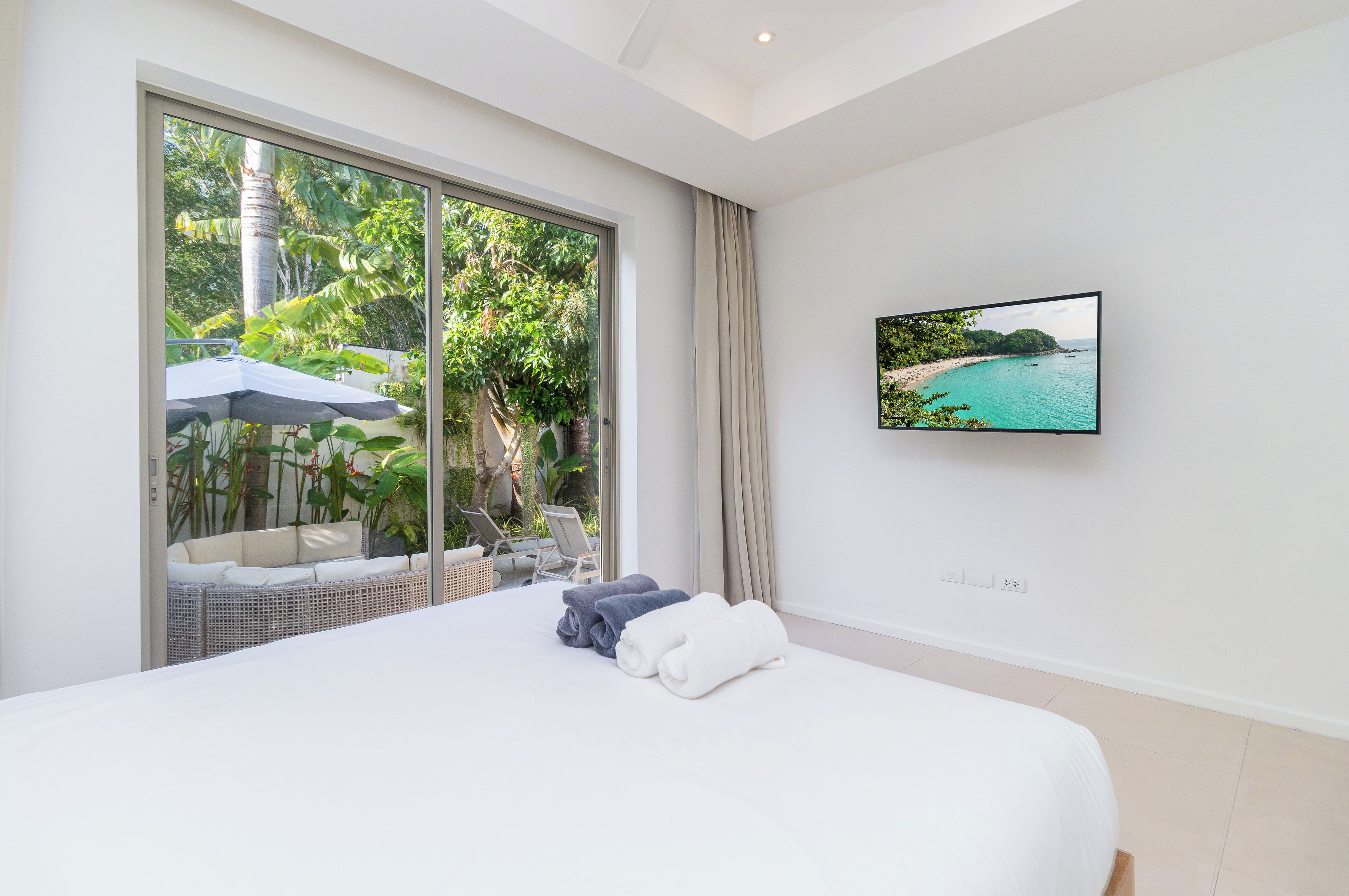 Un dormitorio con una ventana grande, una cama, un televisor en la pared y vistas a la playa.