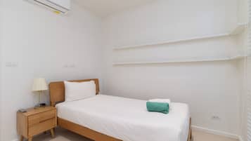 Habitación individual con cama de una sola plaza, cabecera de madera, mesita de noche con lámpara y aire acondicionado instalado en la pared.