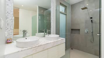 Un baño moderno con dos lavamanos, una cabina de ducha de vidrio y un espejo grande.