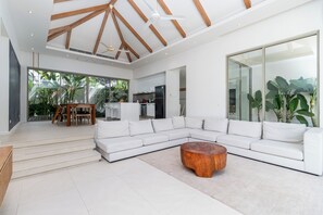 A spacious living room with a white sectional sofa, a wooden coffee table, and a large window offering a view of the outdoors. - Stunning Pool Villa 4 BR - Trichada 24 (Thalang)