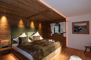 Une chambre dans une cabane en bois, avec un grand lit, une tête de lit et une fenêtre avec des rideaux.