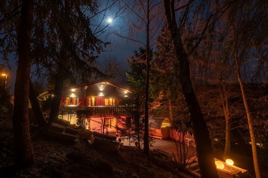 Eine Hütte mit einer Terrasse, umgeben von Bäumen, und ein beleuchteter Weg, der zum Eingang führt.