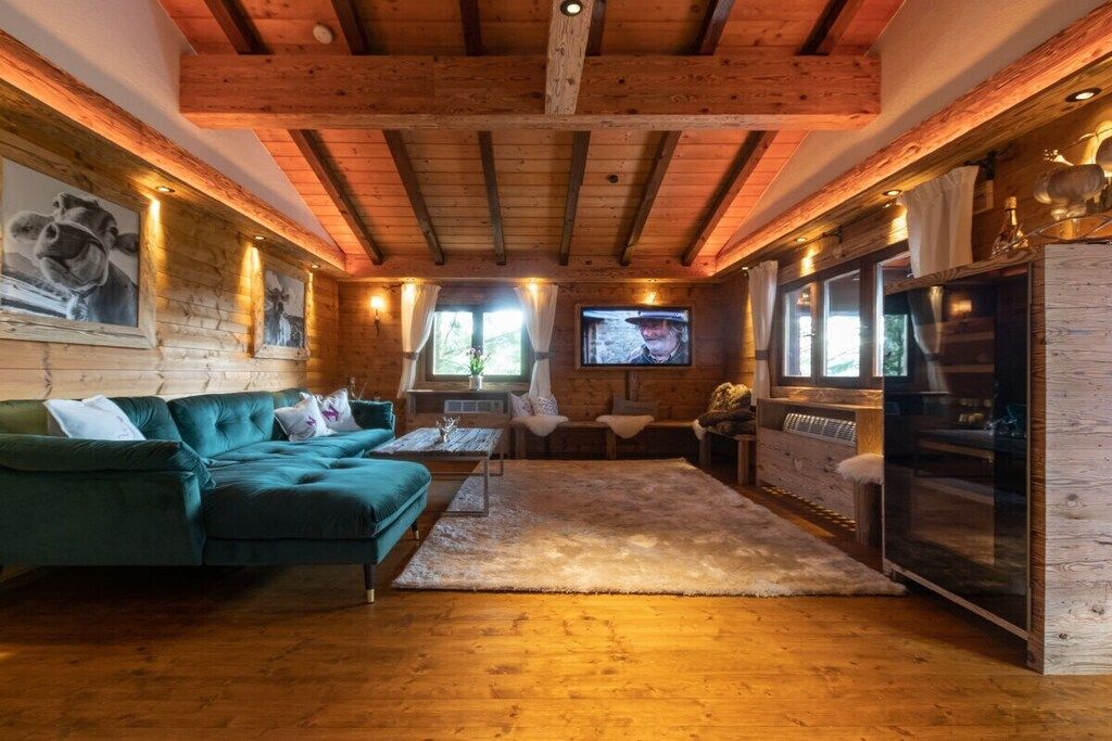 Ein gemütliches Interieur mit Holzbalkendecke, einem grünen Sofa, einem Fernseher und einer Bar.