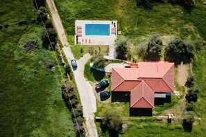 Vue aérienne d’une propriété comprenant une piscine, un bâtiment à toit rouge et une route.