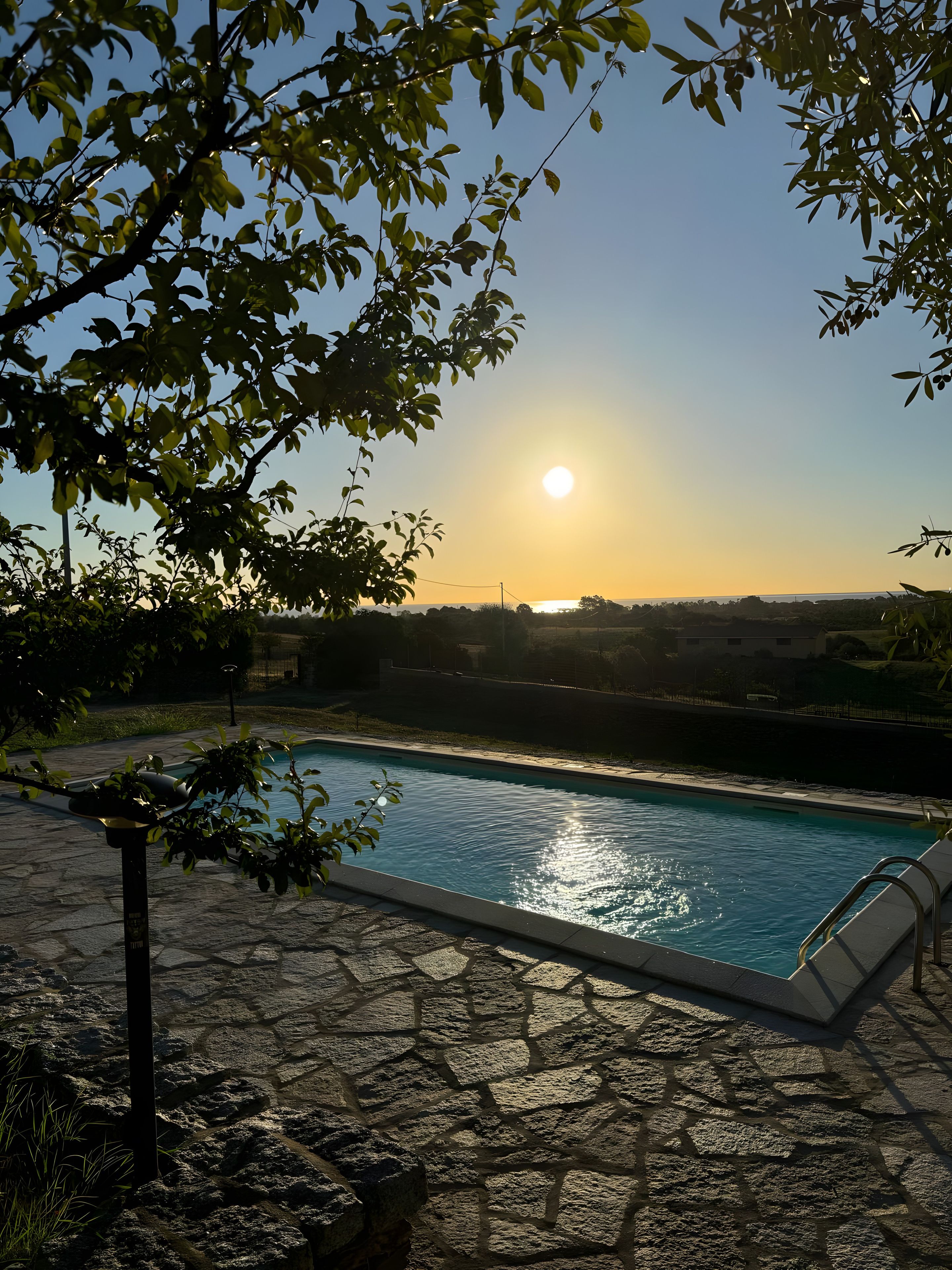 Piscina com piso de pedra, rodeada por vegetação e céu claro.