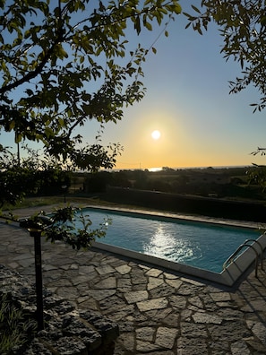 Piscina com piso de pedra, rodeada por vegetação e céu claro.