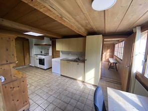 A compact kitchen with basic appliances, a dining area with a table and chairs, and a view through an open door to an outdoor space. - Chalet Legi Ferienhaus, Dusche oder Bad, WC, 4 oder mehr Schlafräume Chalet Legi by Interhome (Adelboden)