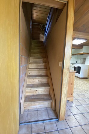 Una scala in legno conduce a una zona cucina con pavimento piastrellato.