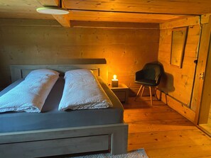 A wooden room with a bed, a chair, and a table with a lamp. - Chalet Legi Ferienhaus, Dusche oder Bad, WC, 4 oder mehr Schlafräume Chalet Legi by Interhome (Adelboden)