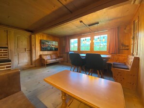 Een houten interieur met een eettafel, stoelen, een bank en een raam met gordijnen.