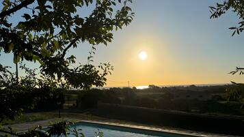 Piscina com piso de pedra, rodeada por vegetação e céu claro.