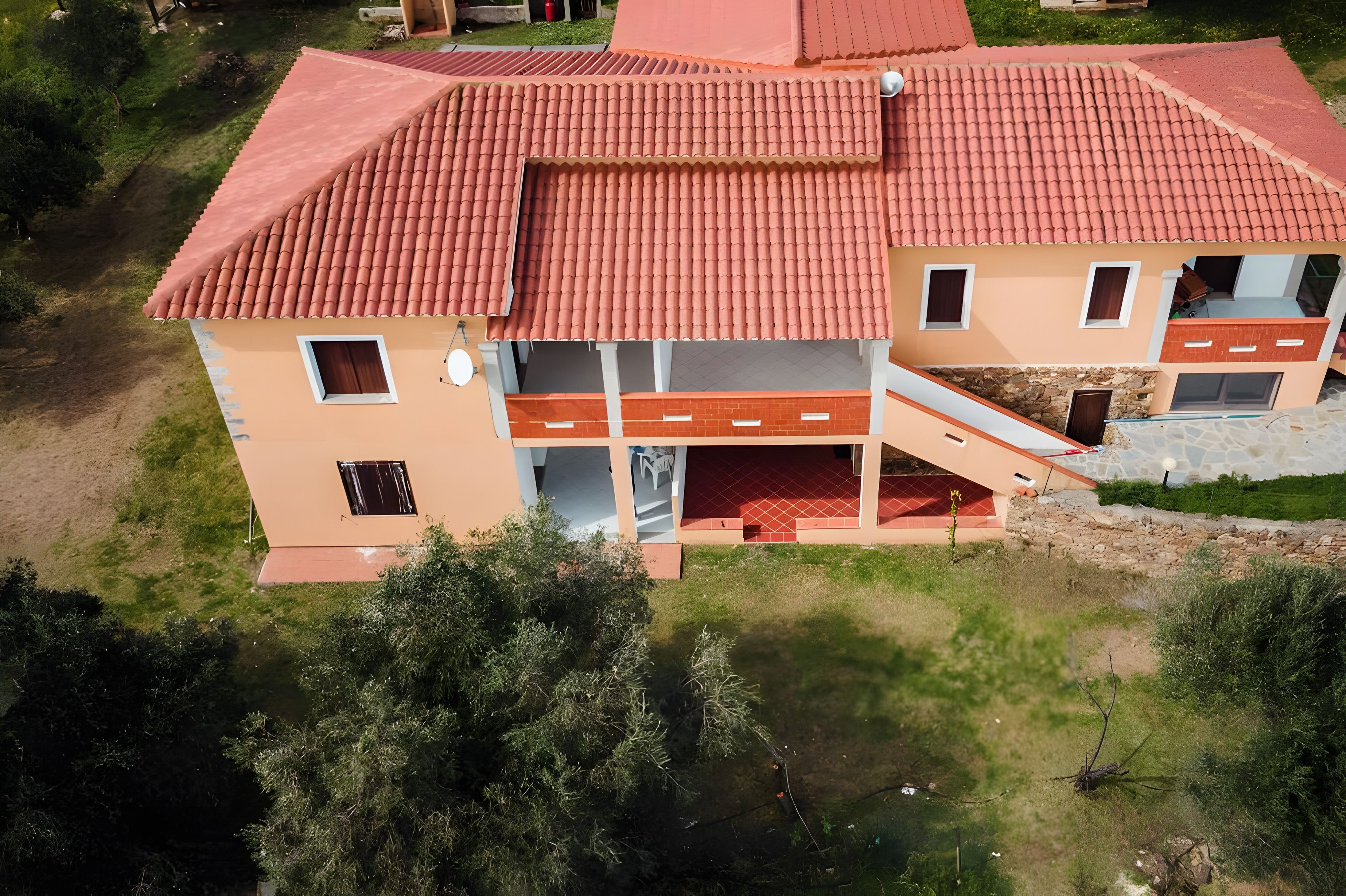A two-story building with a red-tiled roof, a balcony, and a small garden area.