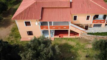 A two-story building with a red-tiled roof, a balcony, and a small garden area.