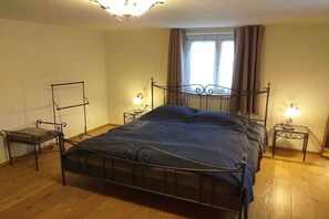 A single-bed room with a metal frame, a bedside table with a lamp, a chair, and a window with curtains. - Holiday home with 4 bedrooms (Altusried)