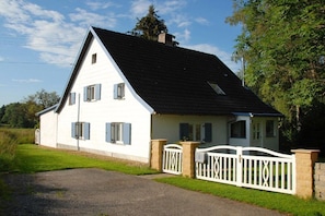 A white house with a black roof, a gated driveway, and a grassy yard. - Holiday home with 4 bedrooms (Altusried)