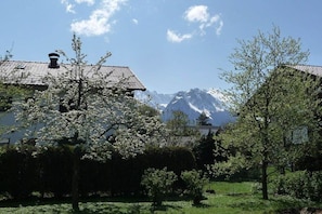 A residential area with a house, a tree with white blossoms, and a mountain range in the background. - Wank in the house of Georg (Garmisch-Partenkirchen)