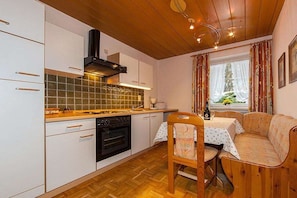 A compact kitchen with white cabinets, a black stove, and a window with curtains. - Wank in the house of Georg (Garmisch-Partenkirchen)