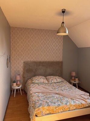 Ein Schlafzimmer mit einem Bett, einem Kopfteil, einer Hängelampe, einem kleinen Tisch mit Lampe und einer Zimmerpflanze.
