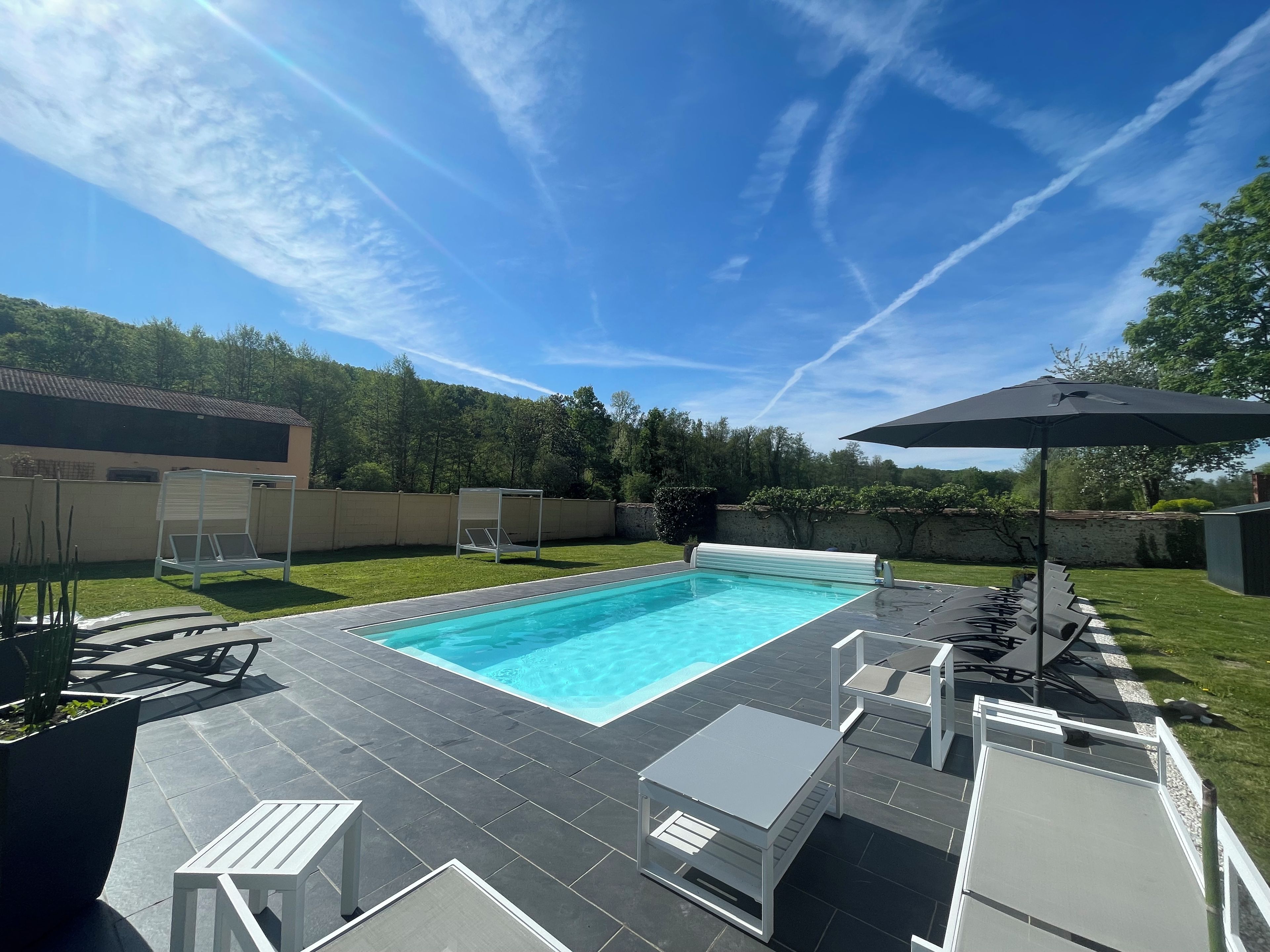 Une piscine dotée d’une terrasse carrelée, entourée de mobilier d’extérieur et d’un espace abrité.